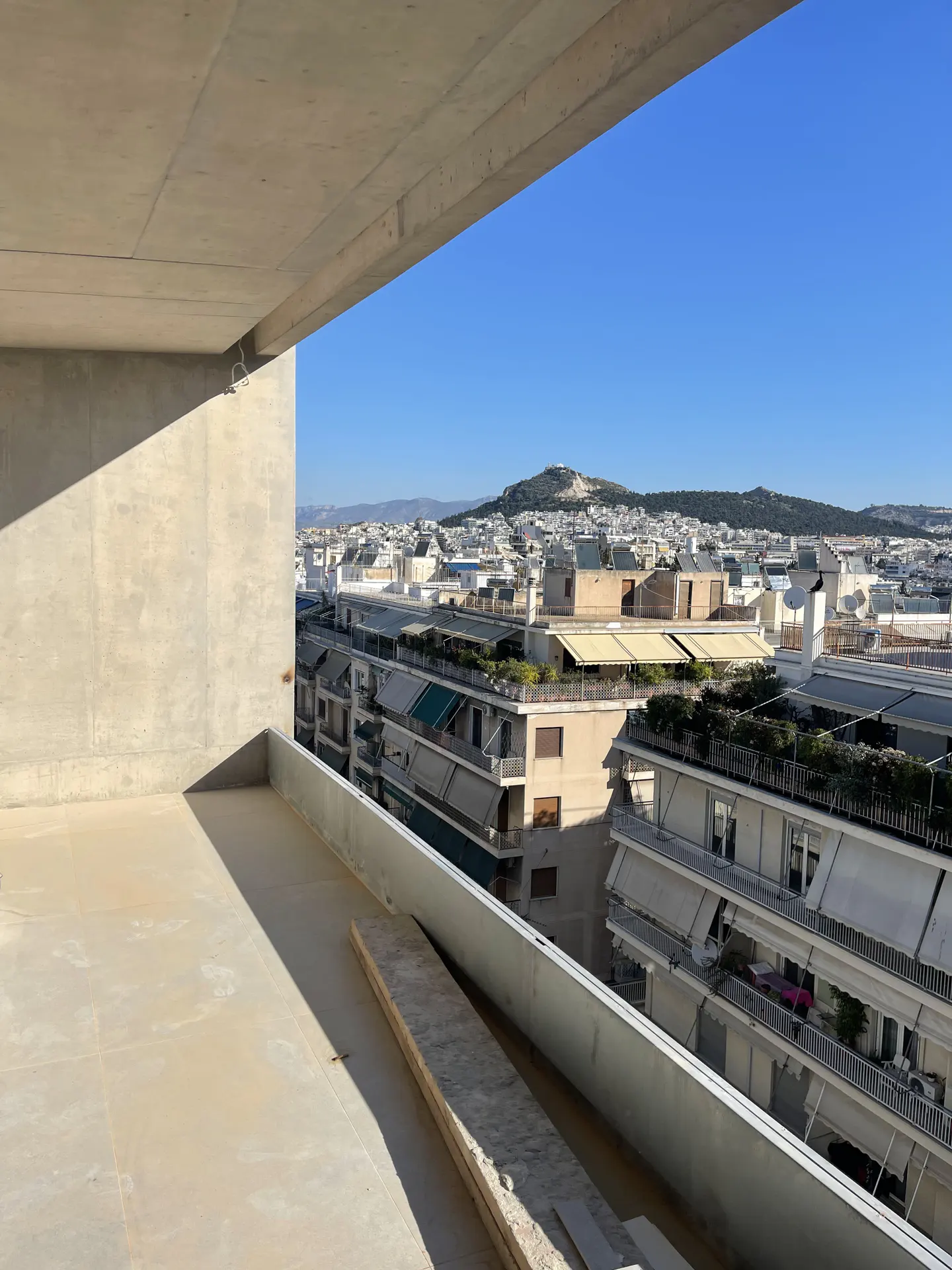 View from a balcony overlooking a city with white buildings and a mountain under a blue sky.