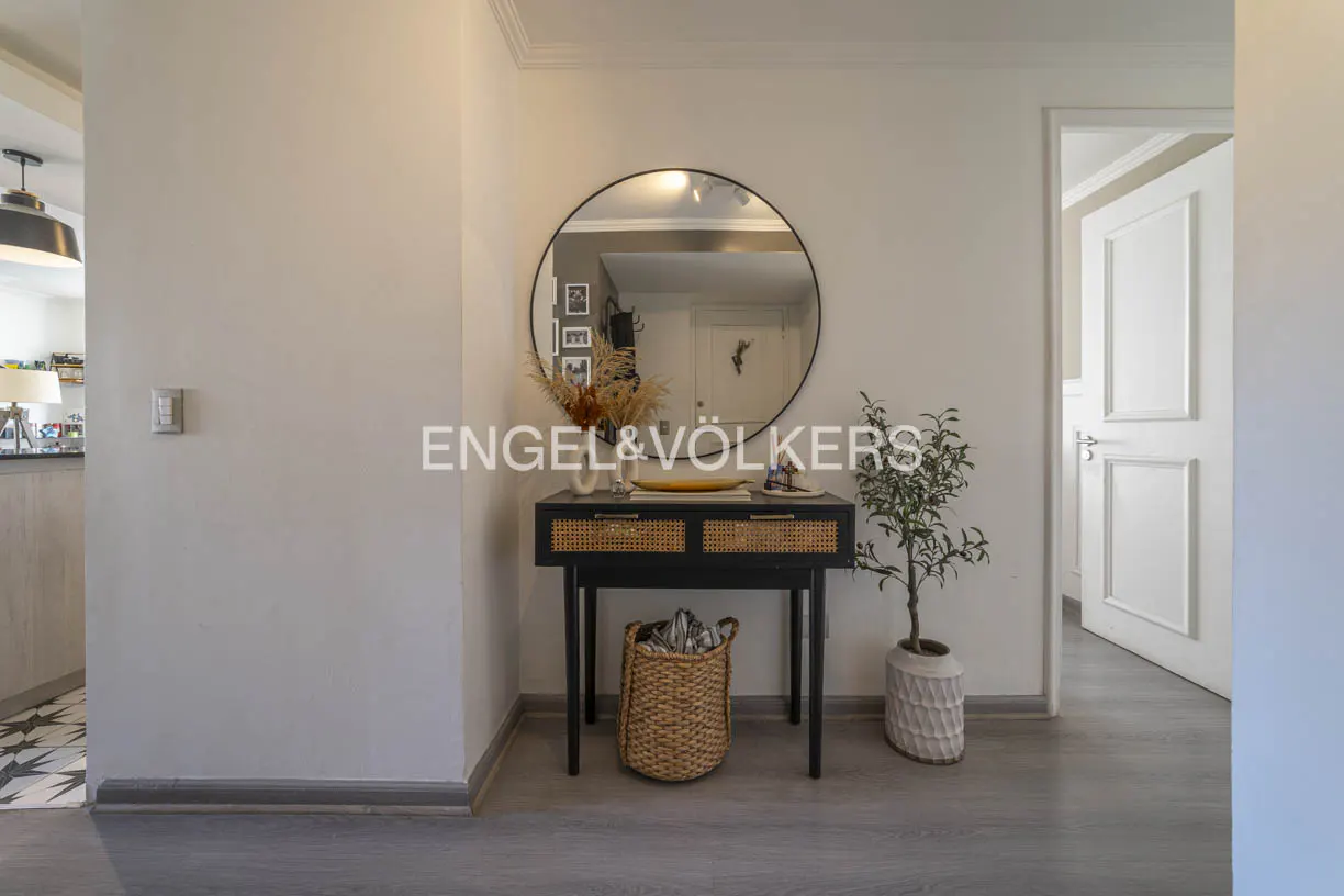 Entryway with a black console table, round mirror, plant, and woven basket. A white door is slightly ajar. Gray wood floors.