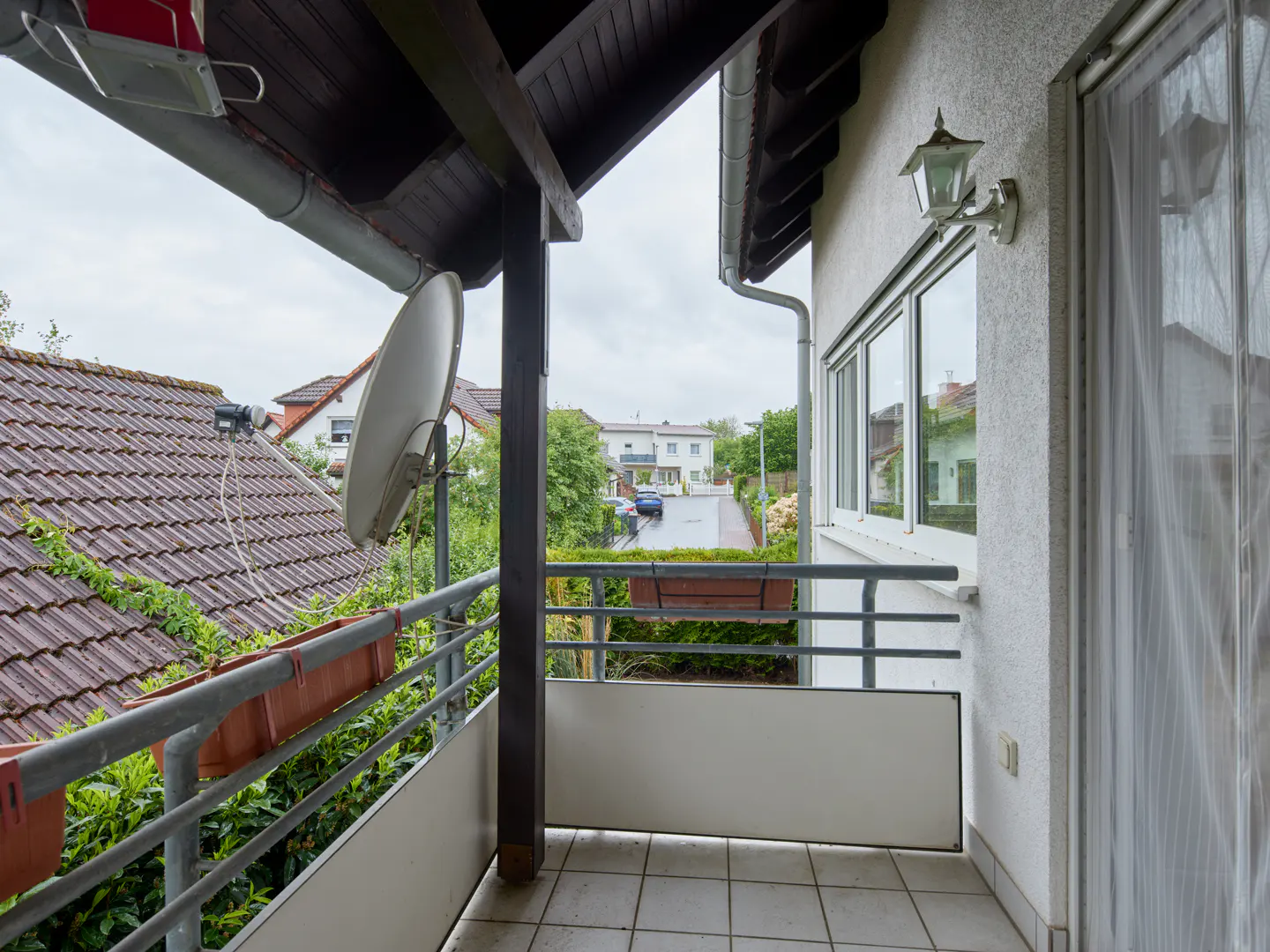 View from a balcony with gray railings, a satellite dish, and a view of a residential street.