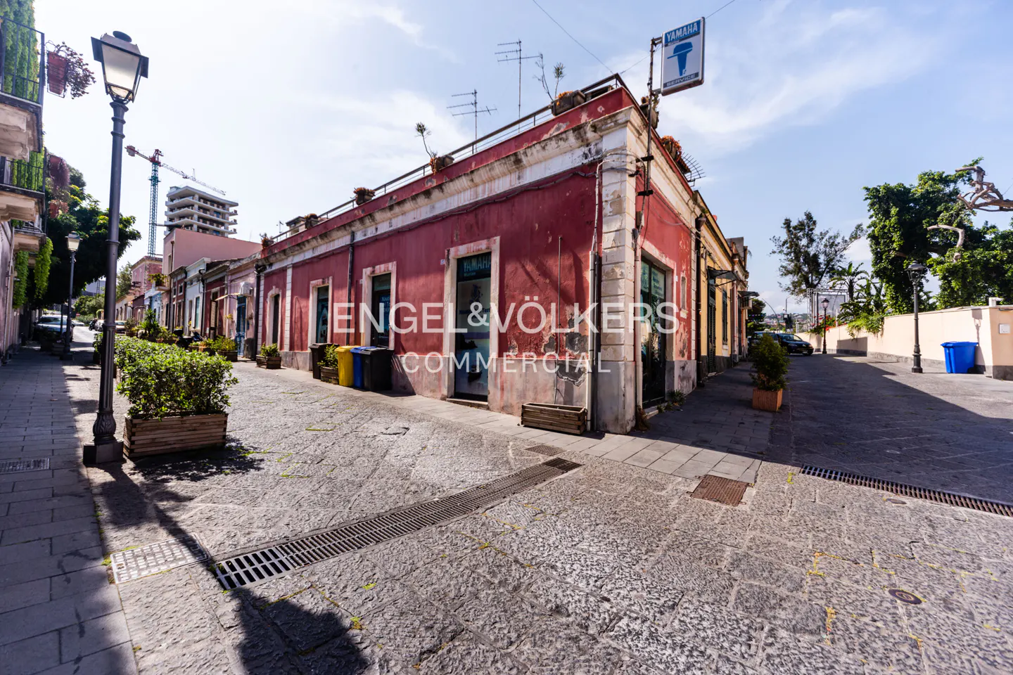 Street view of a red building with a Yamaha sign, cobblestone road, and Engel & Völkers Commercial logo.
