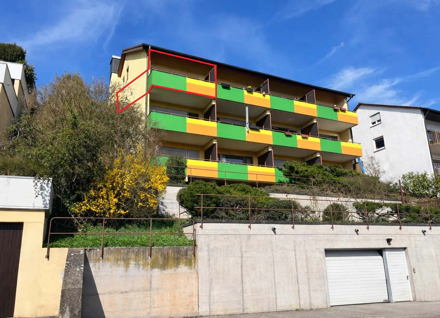 Exterior view of a three-story apartment building with green and yellow balconies on a sunny day.