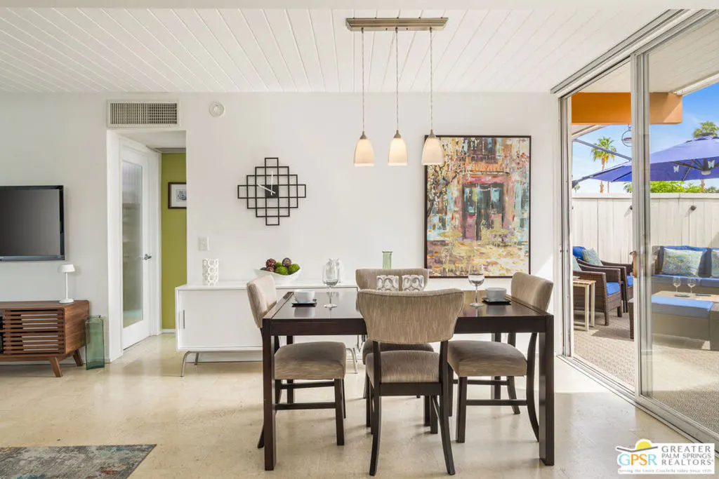 A dining area with a dark wood table, four chairs, and a sliding glass door to a patio with blue furniture.