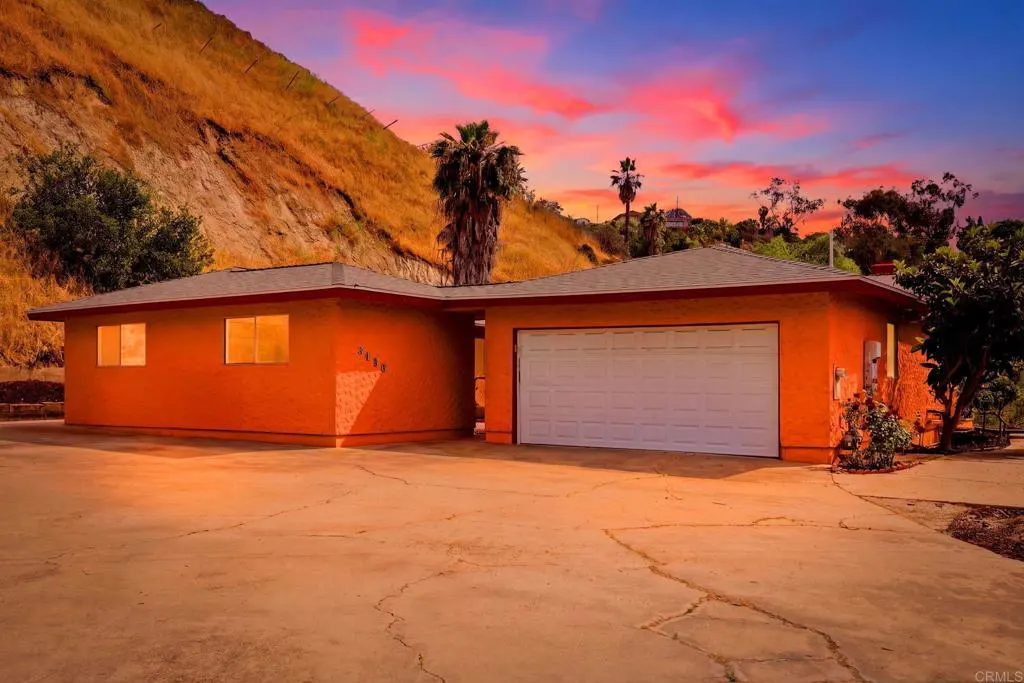 Orange single-story house with a white garage door, set against a hillside and a colorful sunset sky.