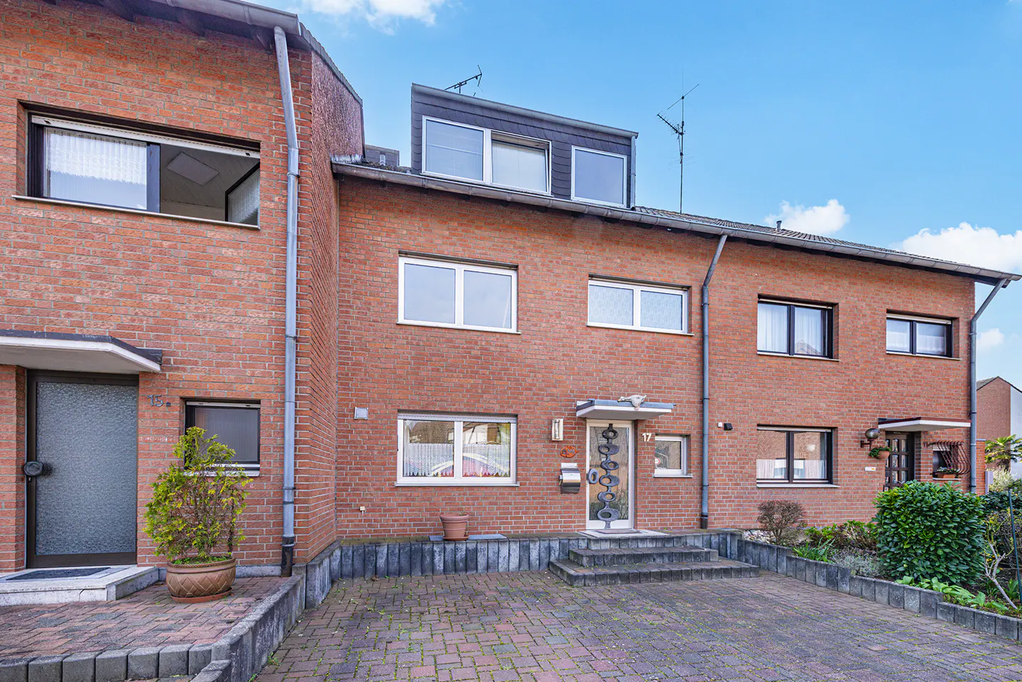 Exterior of brick townhouses with a brick driveway and blue sky.