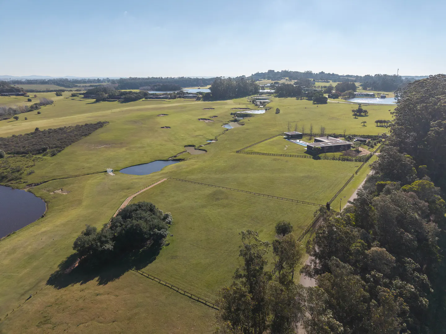 Aerial view of a large green property with ponds, trees, and a modern house.