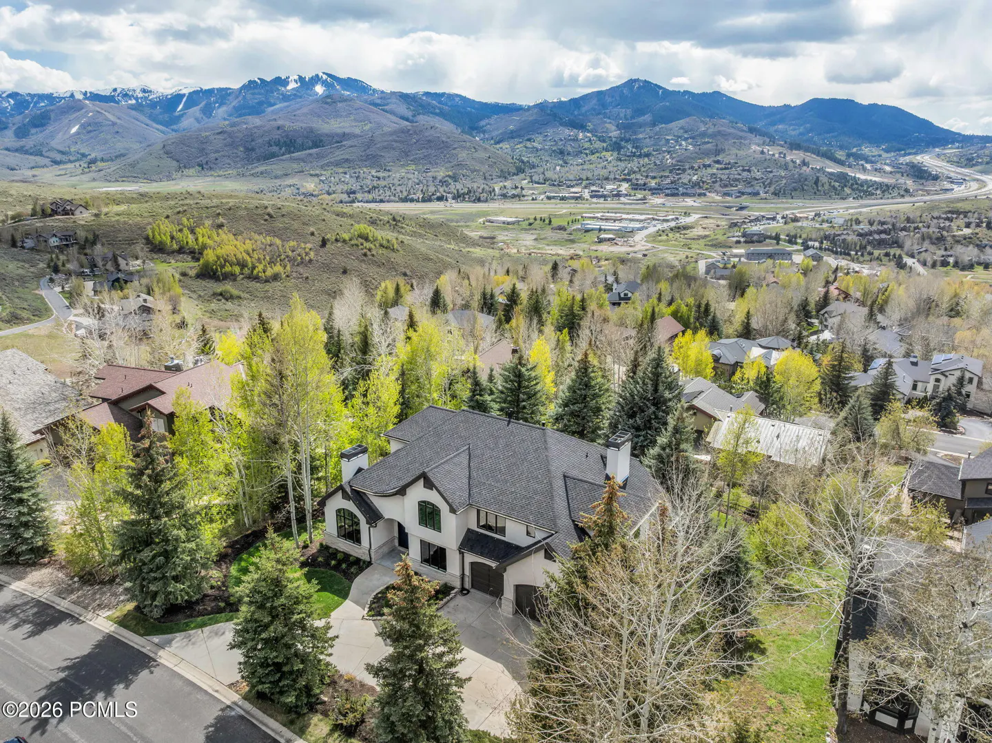 Aerial view of a large, white house with a dark gray roof, surrounded by green trees and mountains in the background.