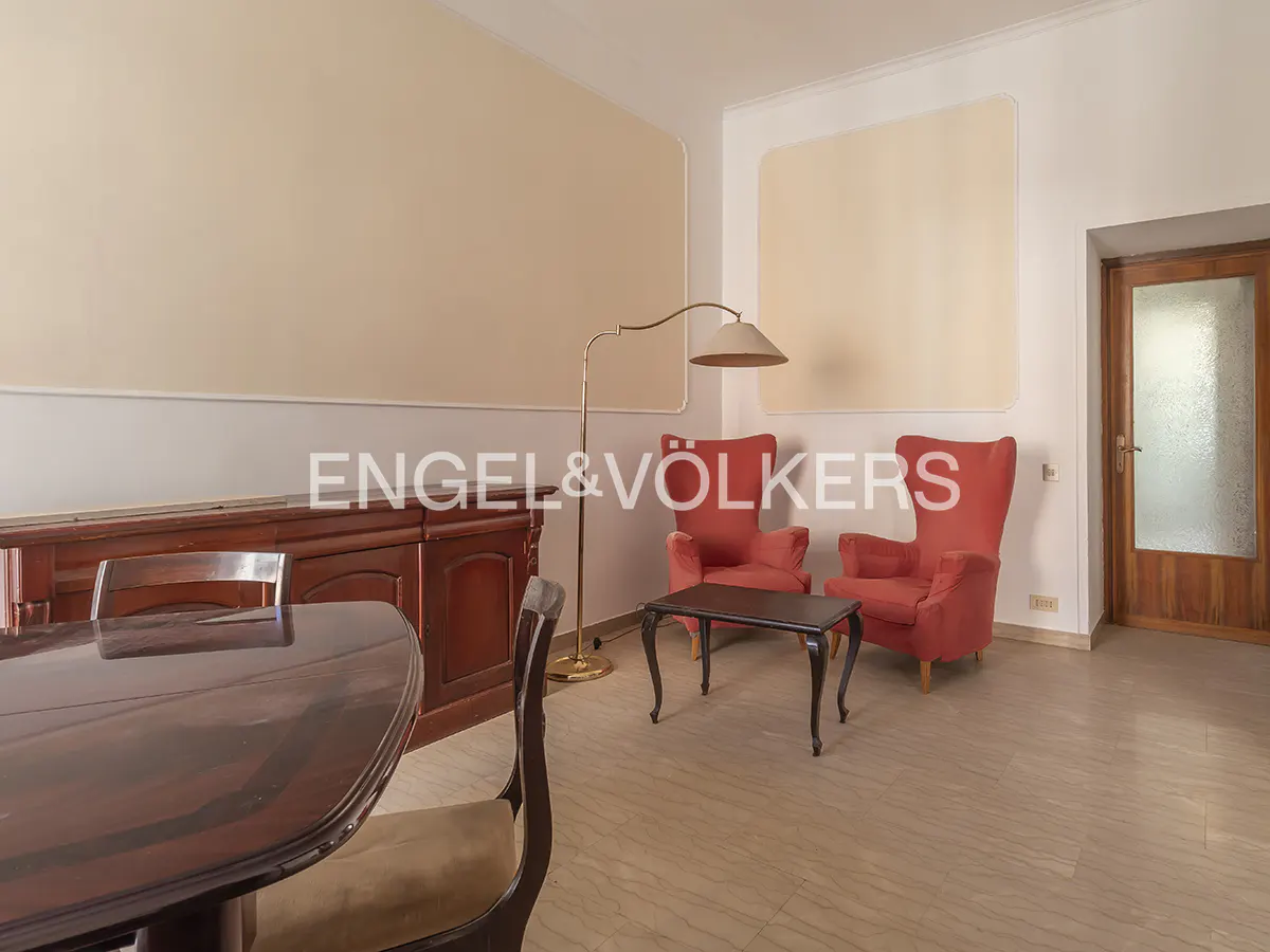 A living room with a dark wood table, two red armchairs, a floor lamp, and a wood cabinet.