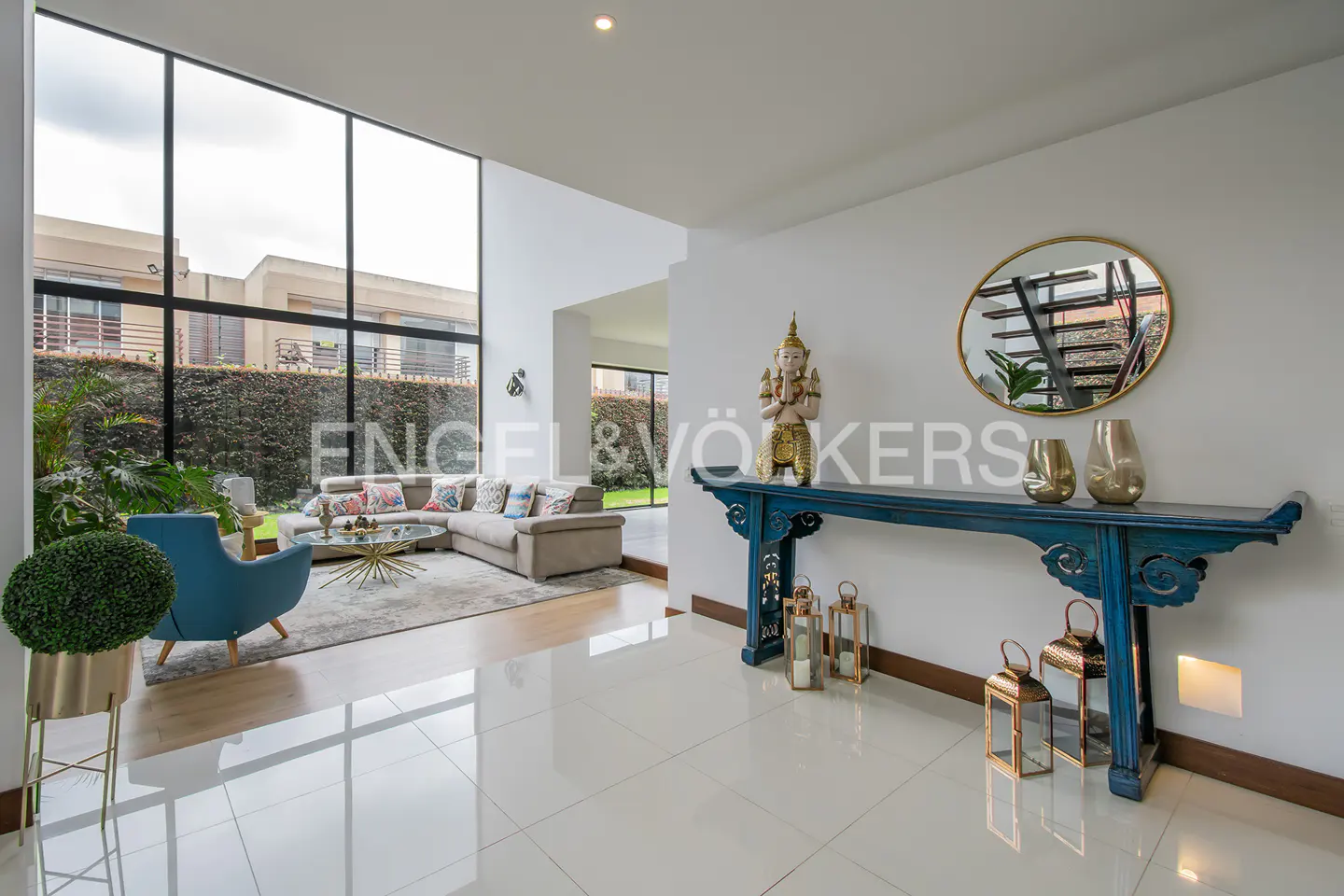 Modern living room with floor-to-ceiling windows, blue accent chair, beige sofa, and a blue console table with decor.