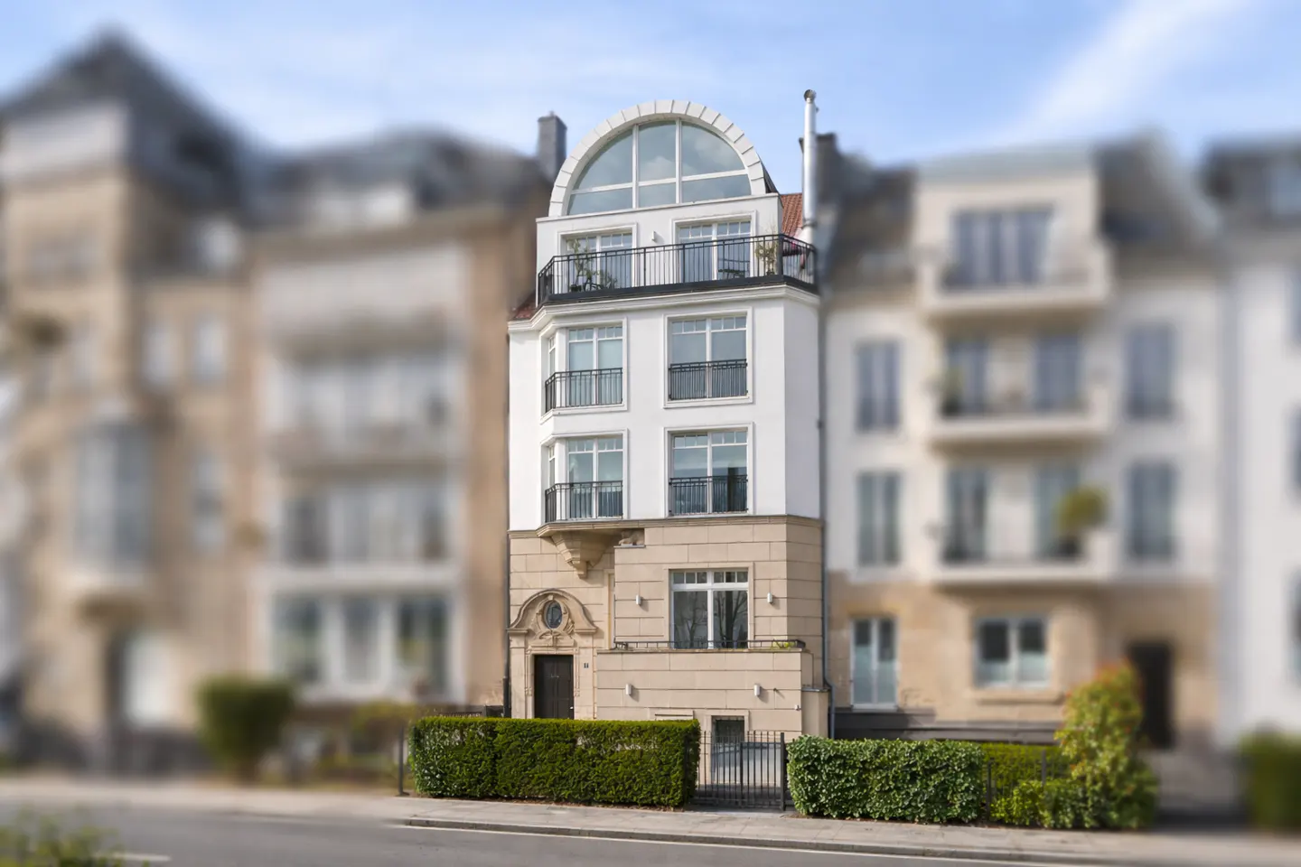 A tall, narrow, white and tan building with a rounded top and black balconies.