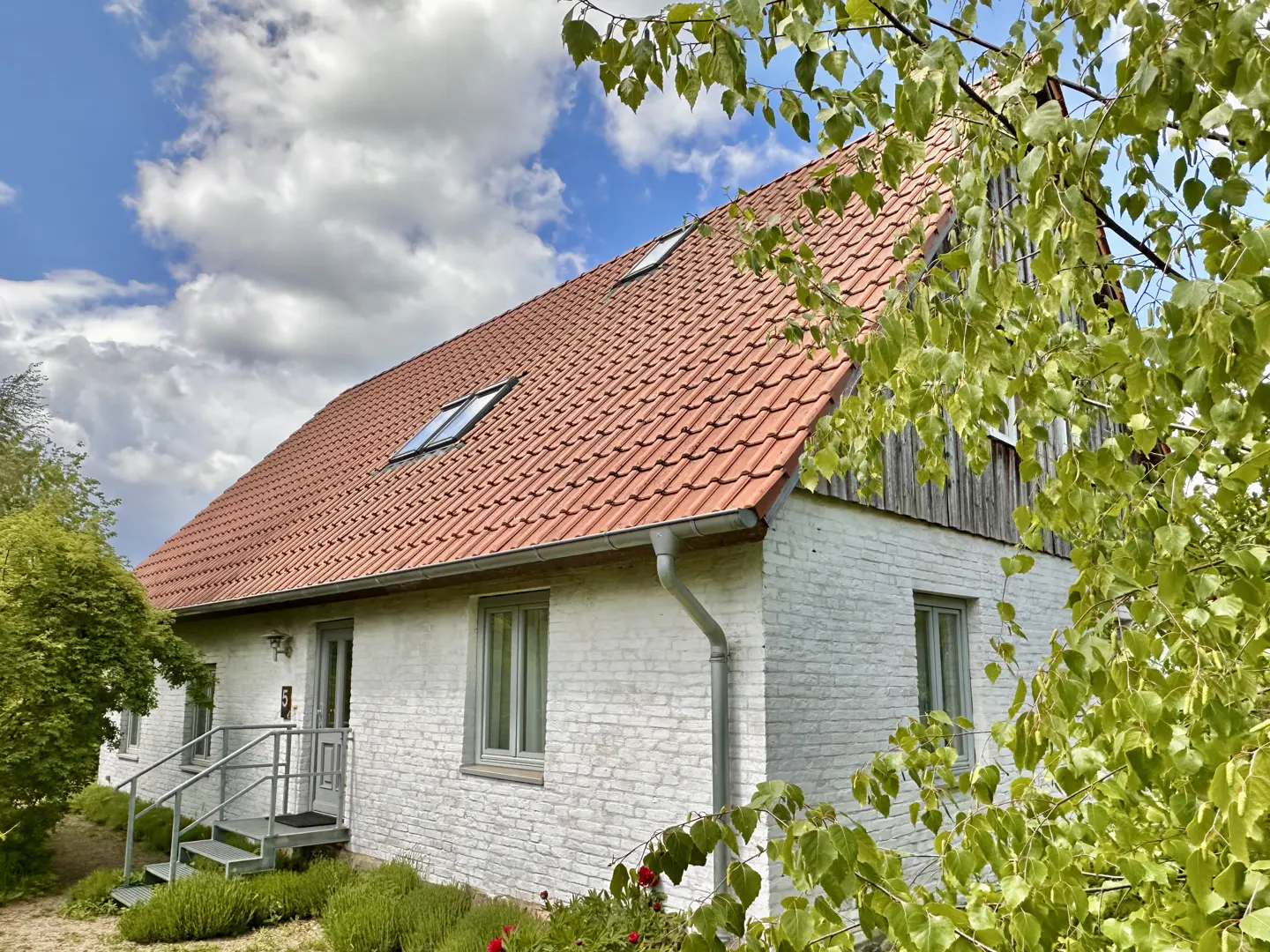 Exterior view of a two-story white brick house with a red tile roof and green trees.