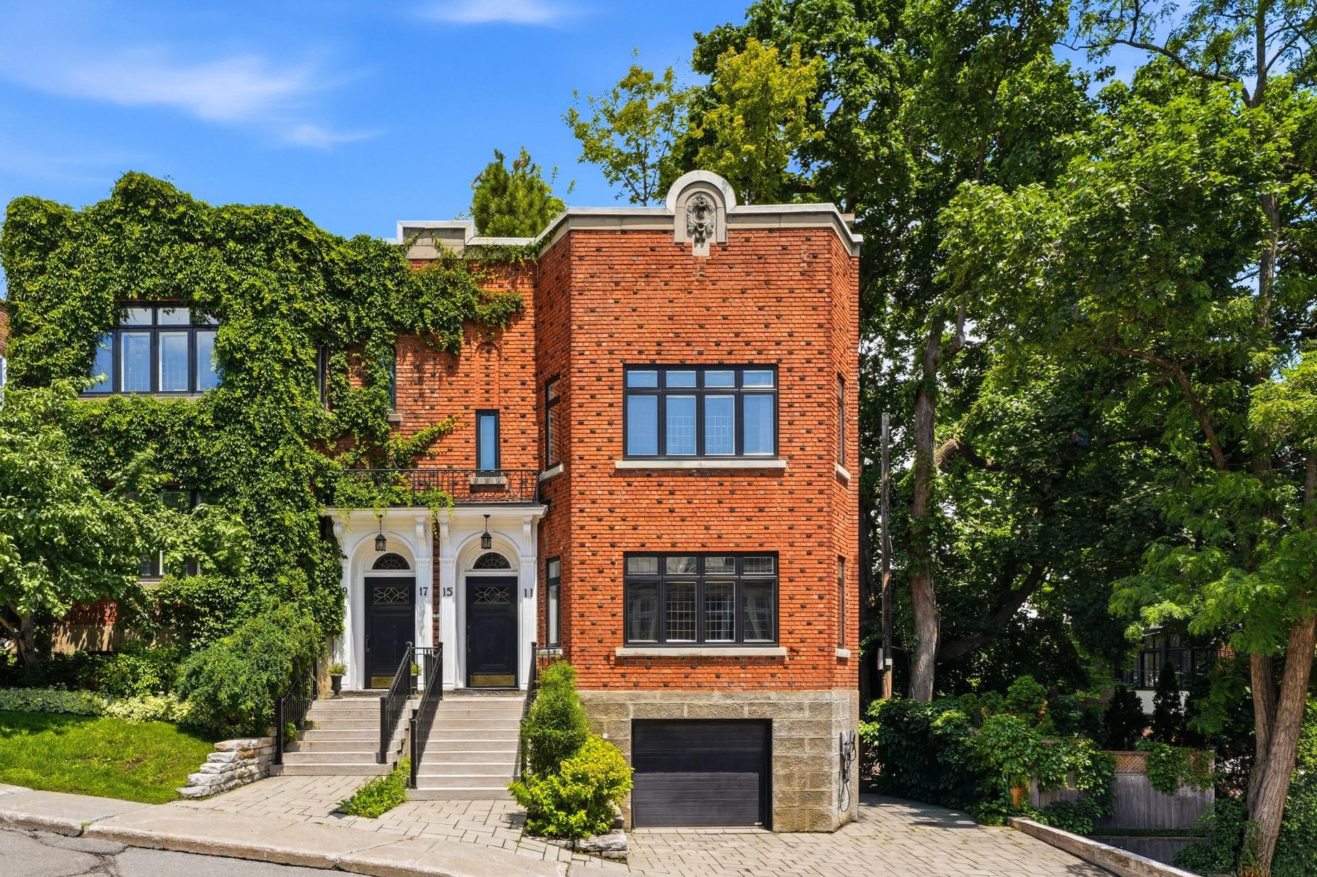 A red brick duplex with a stone base, black trim, ivy-covered walls, and a private garage under a bright blue sky.