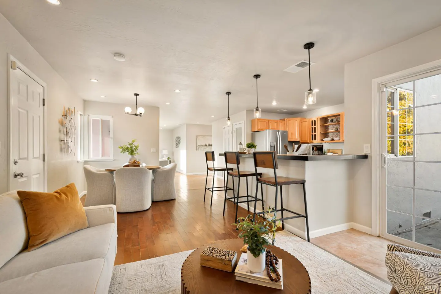 Open-concept living space with wood floors, a dining table, kitchen island with stools, and a white sofa with an orange pillow.