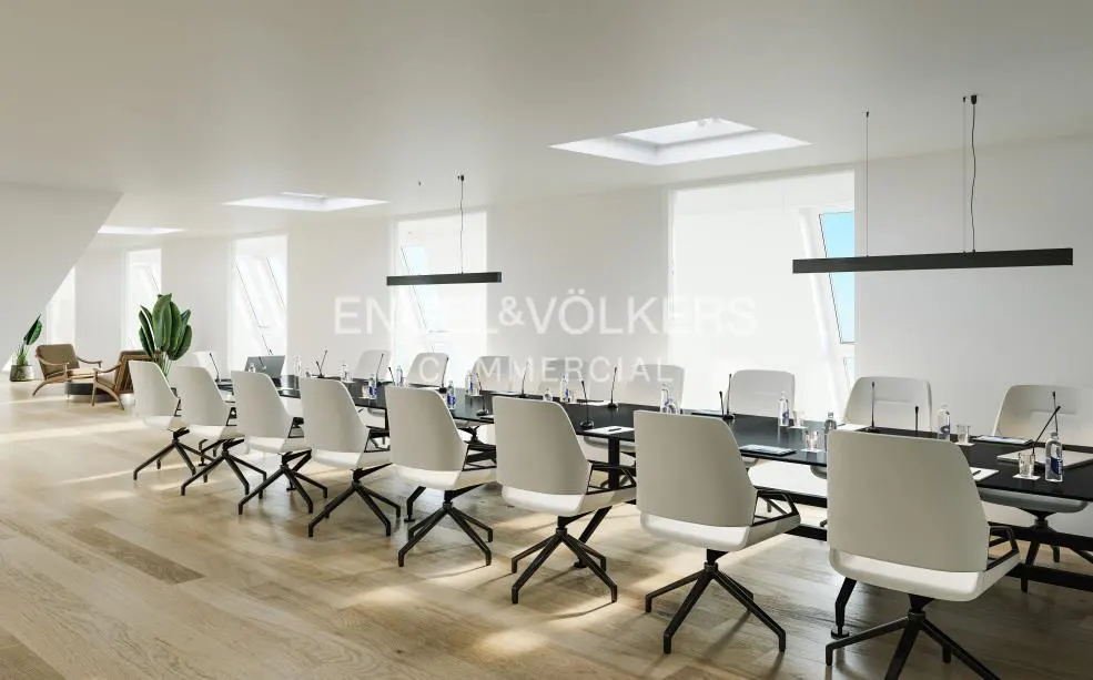 Bright, modern conference room with a long black table, white chairs, and skylights. Engel & Völkers Commercial logo in the background.