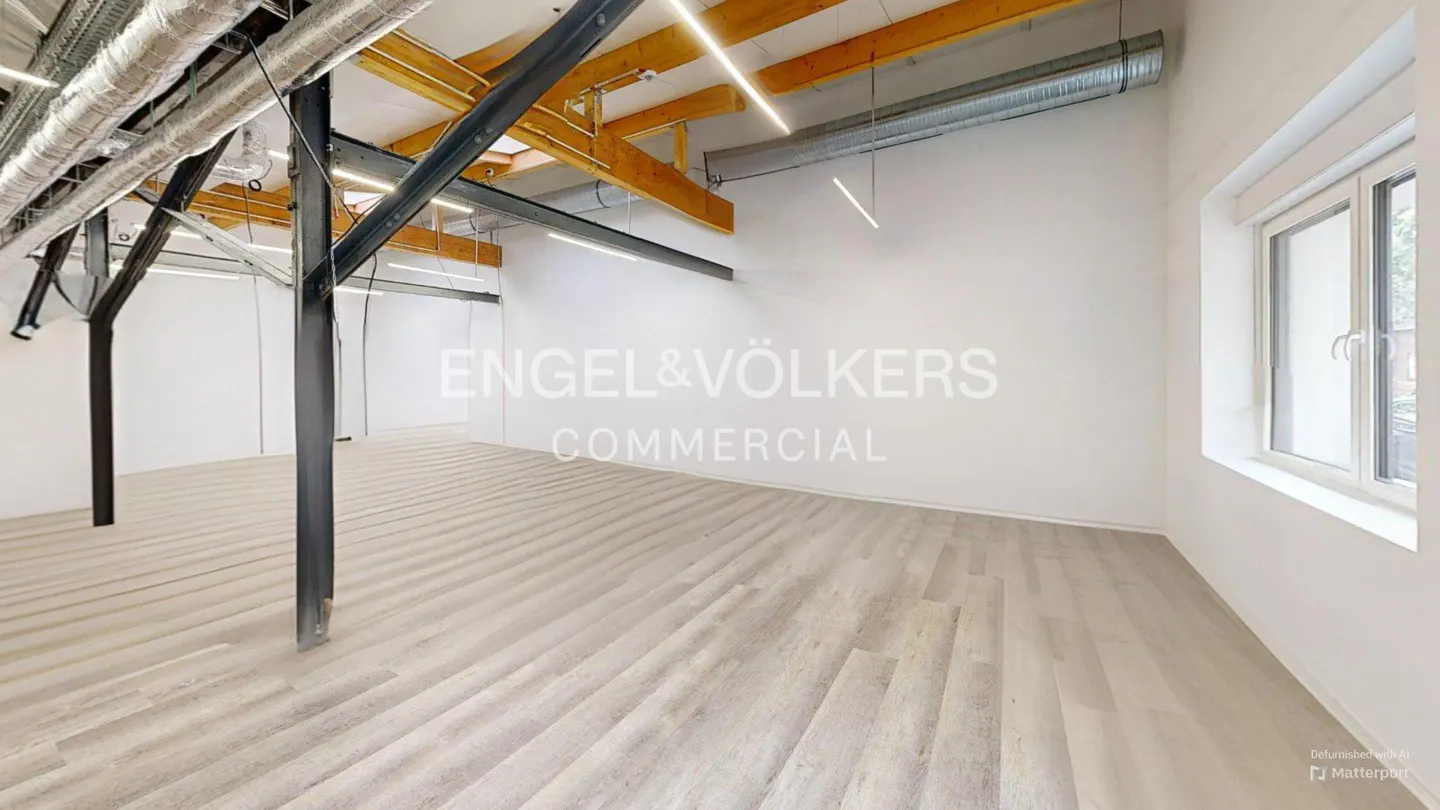 Empty commercial space with light wood floors, white walls, and exposed ceiling beams. Engel & Völkers logo on the wall.