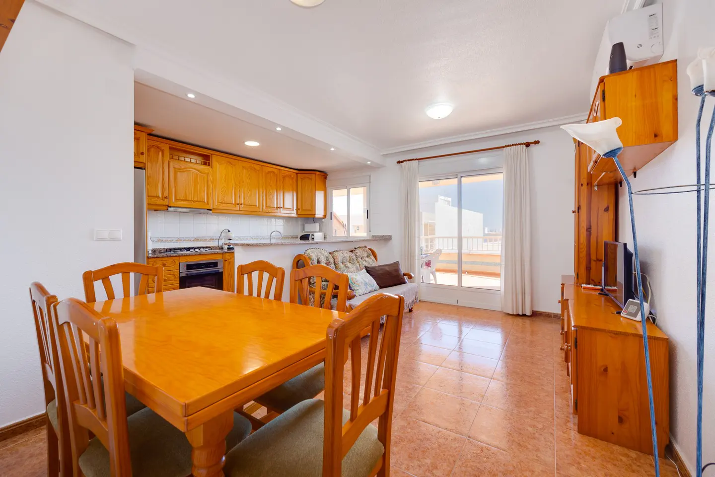 Bright living room with wood dining table, kitchen cabinets, and sliding glass doors to a balcony.
