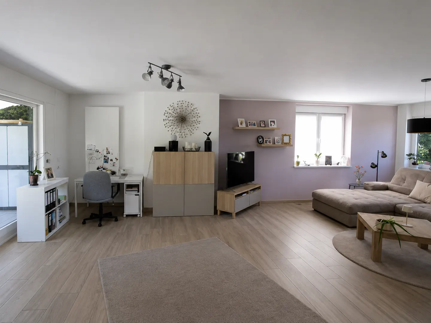 Spacious living room with light wood floors, a beige sectional sofa, a home office area, and a lavender accent wall.