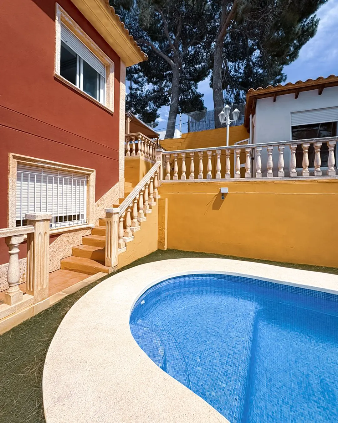 Exterior view of a two-story house with a blue tiled pool, orange walls, and stone stairs with balustrades.