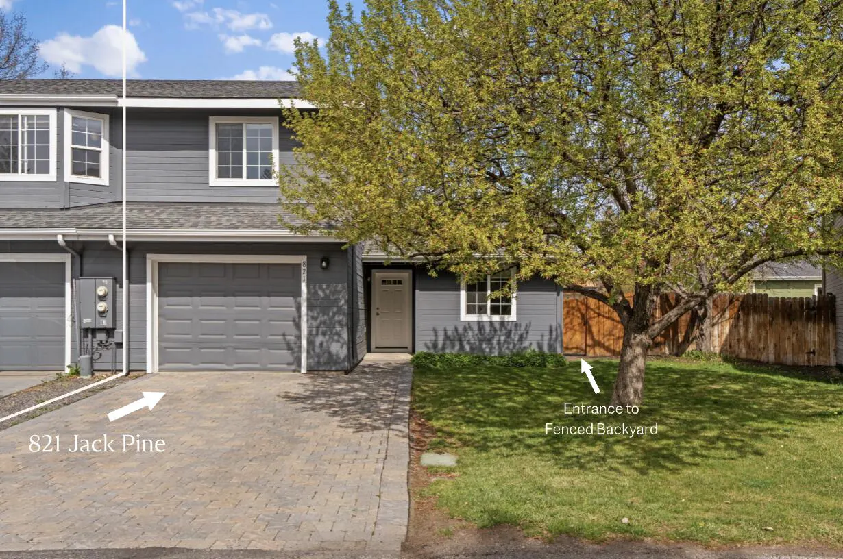 Gray two-story townhouse with a garage and a brick driveway. A large tree shades the front yard.