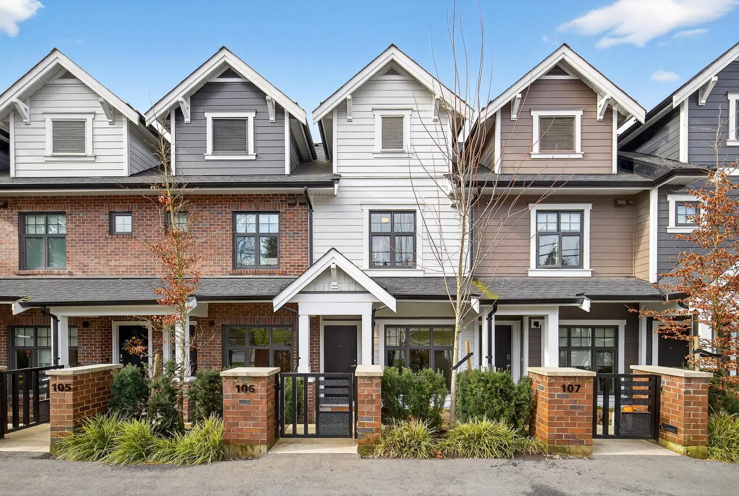 Exterior view of a row of modern townhouses with brick and siding facades, featuring unit numbers 105, 106, and 107.
