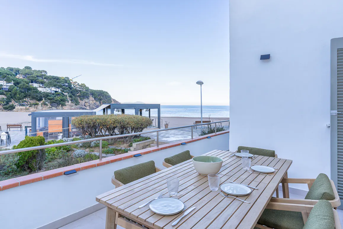Outdoor dining area with a wooden table set for a meal, overlooking a beach and ocean view.