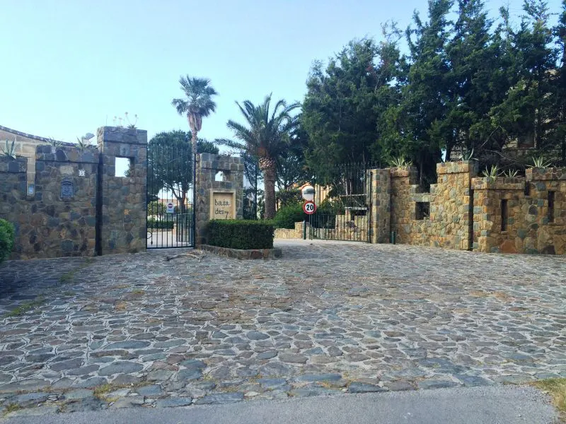 Gated entrance to Baja del Rey estate with stone walls, palm trees, and cobblestone driveway.