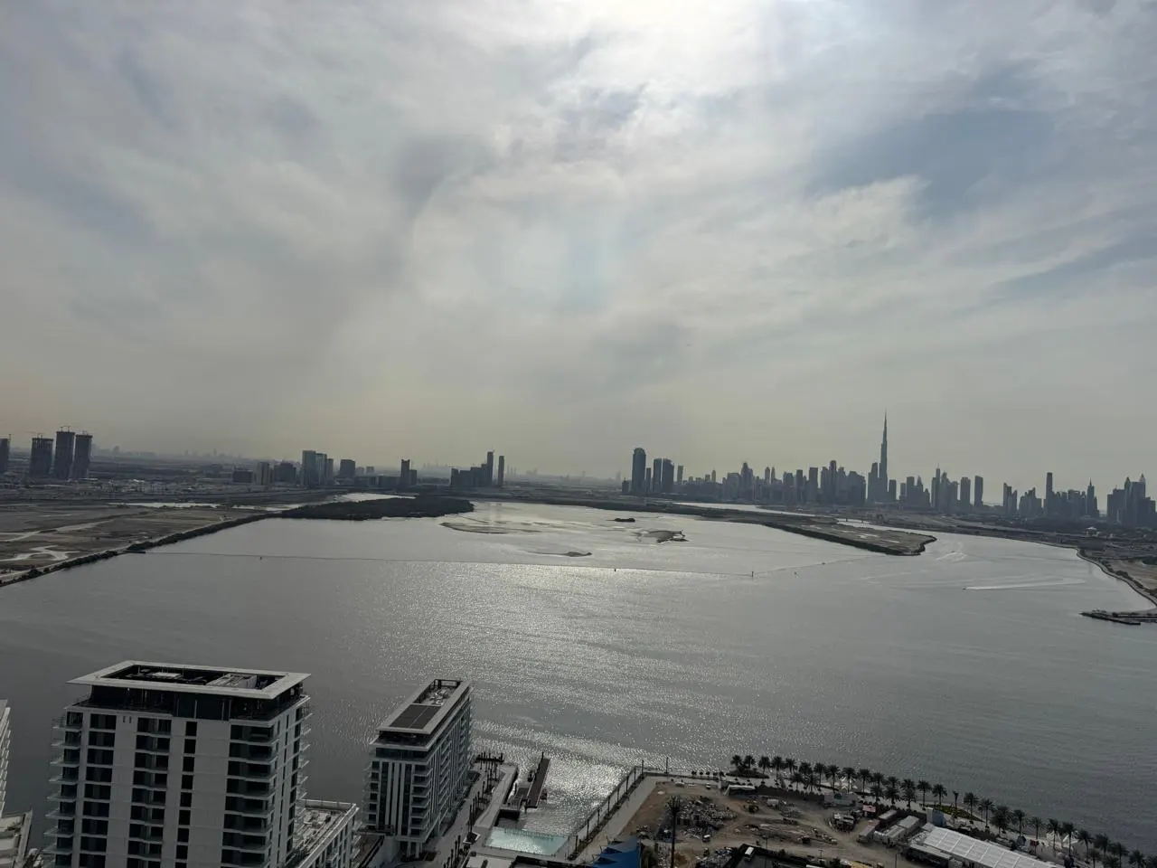 View of Dubai skyline from a high-rise building, overlooking a bay with shimmering water under a cloudy sky.