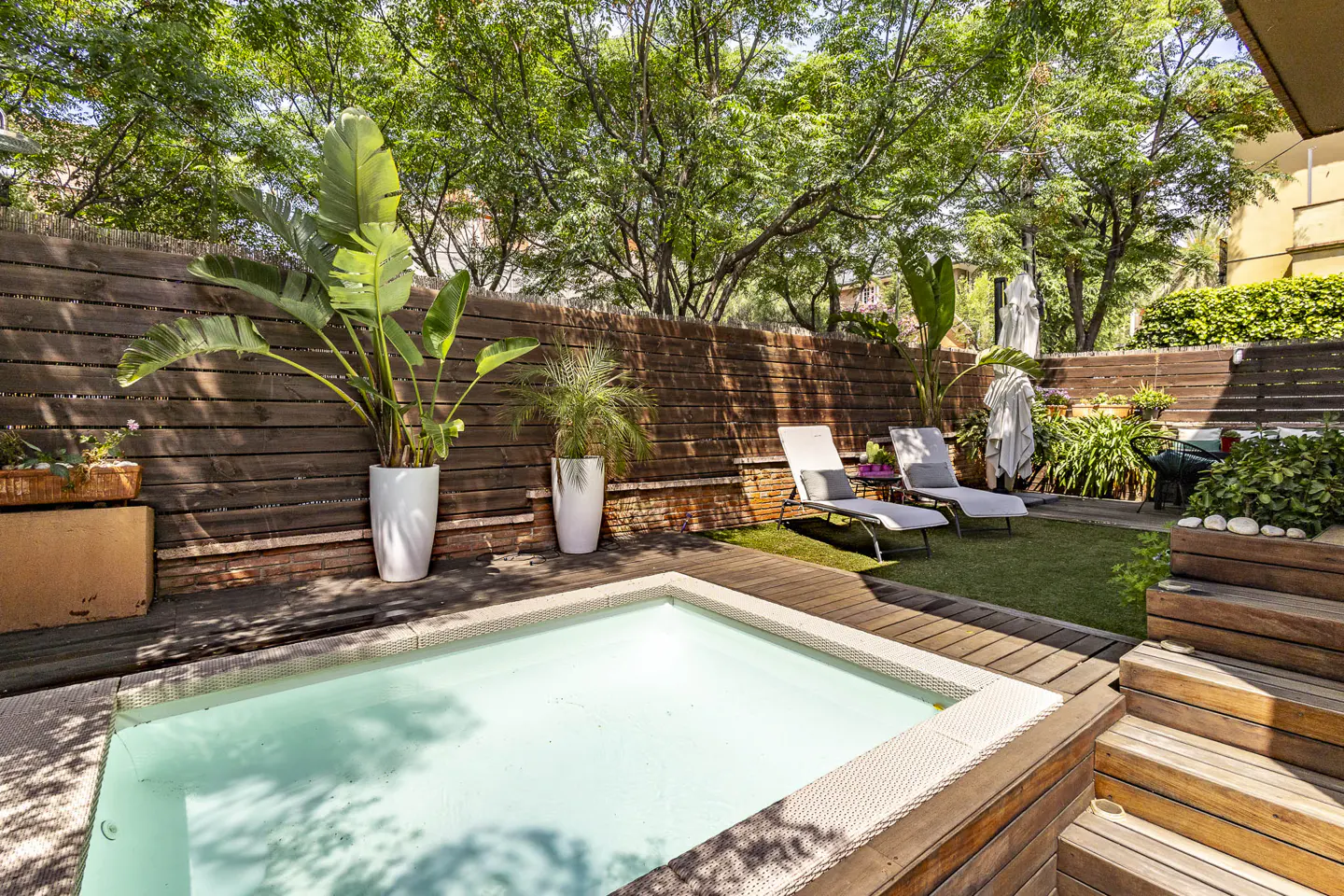 Backyard with a small pool, wooden deck, lounge chairs, and lush greenery.