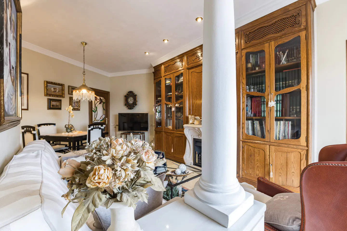 A living room with a white column, wooden cabinets, a fireplace, and a dining area.