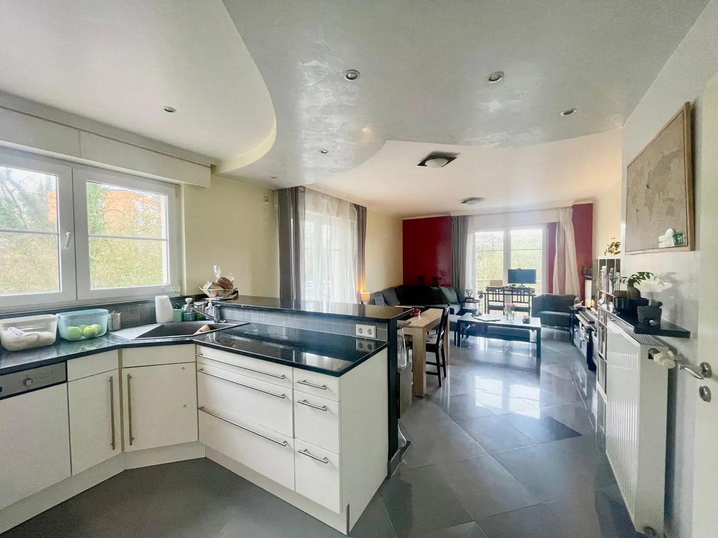 Open concept kitchen and living room with white cabinets, black countertops, and gray tile flooring.