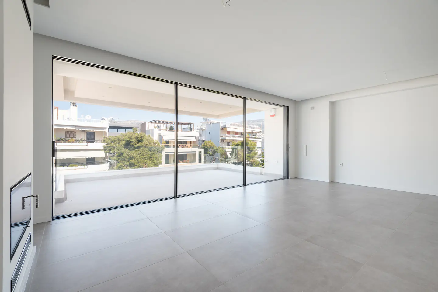 Bright, empty room with gray tile floor and large sliding glass doors to a balcony with city views.