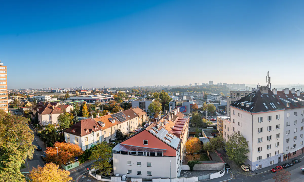 High-angle view of a city neighborhood with colorful buildings, autumn trees, and a clear blue sky.
