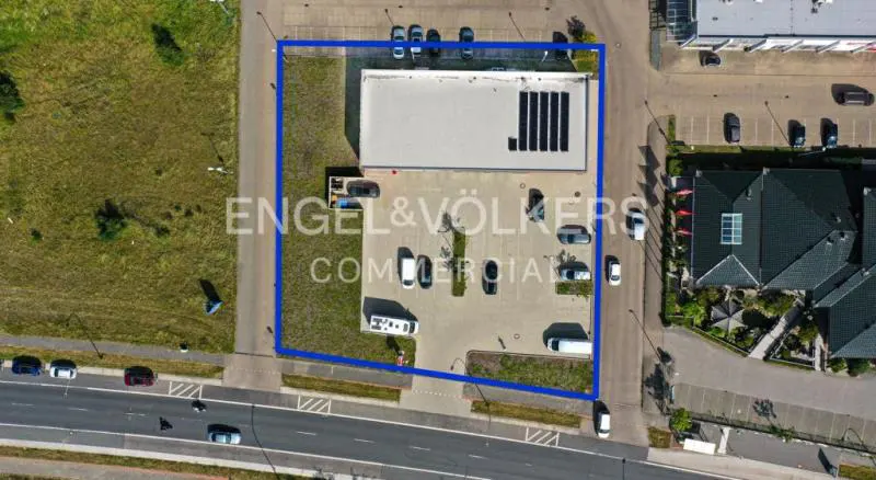Aerial view of a commercial building with a parking lot, outlined in blue, next to a road and green space.
