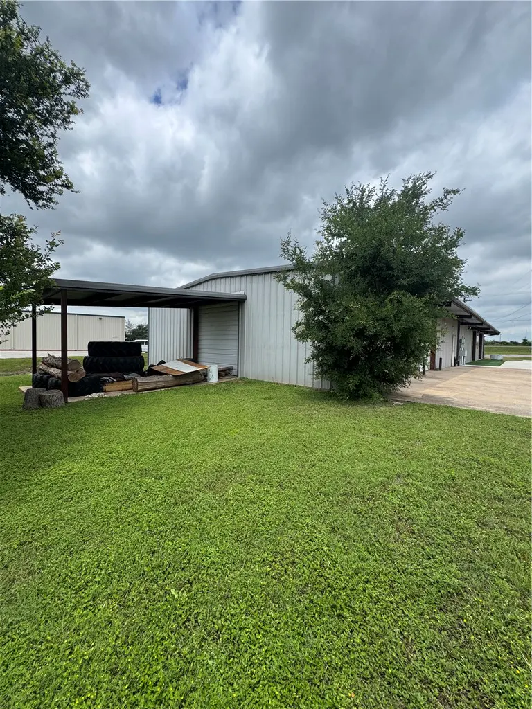 A metal warehouse building with a covered side area, green lawn, and cloudy sky.