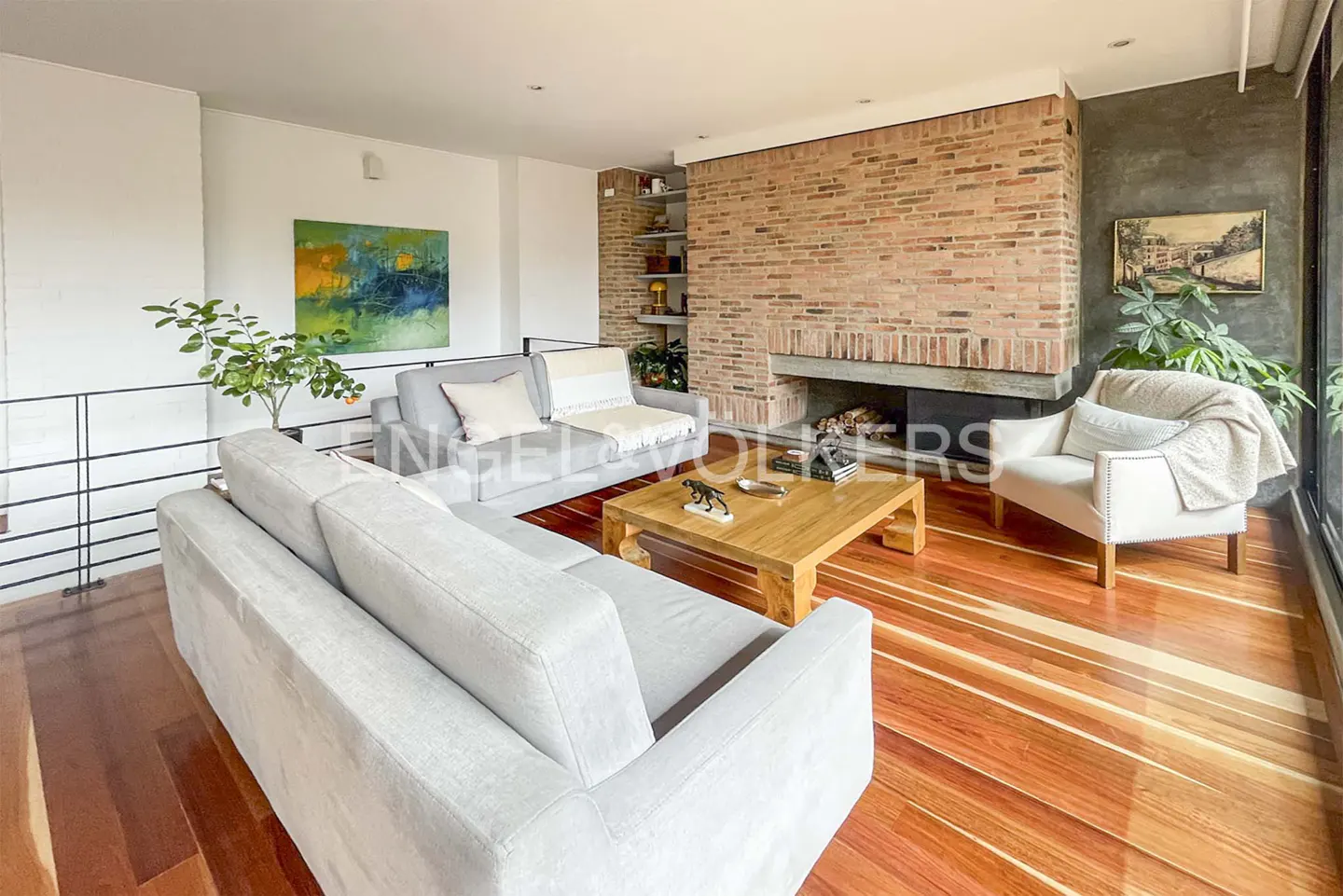 Living room with hardwood floors, gray sofas, brick fireplace, and a wooden coffee table. An abstract painting hangs on the wall.