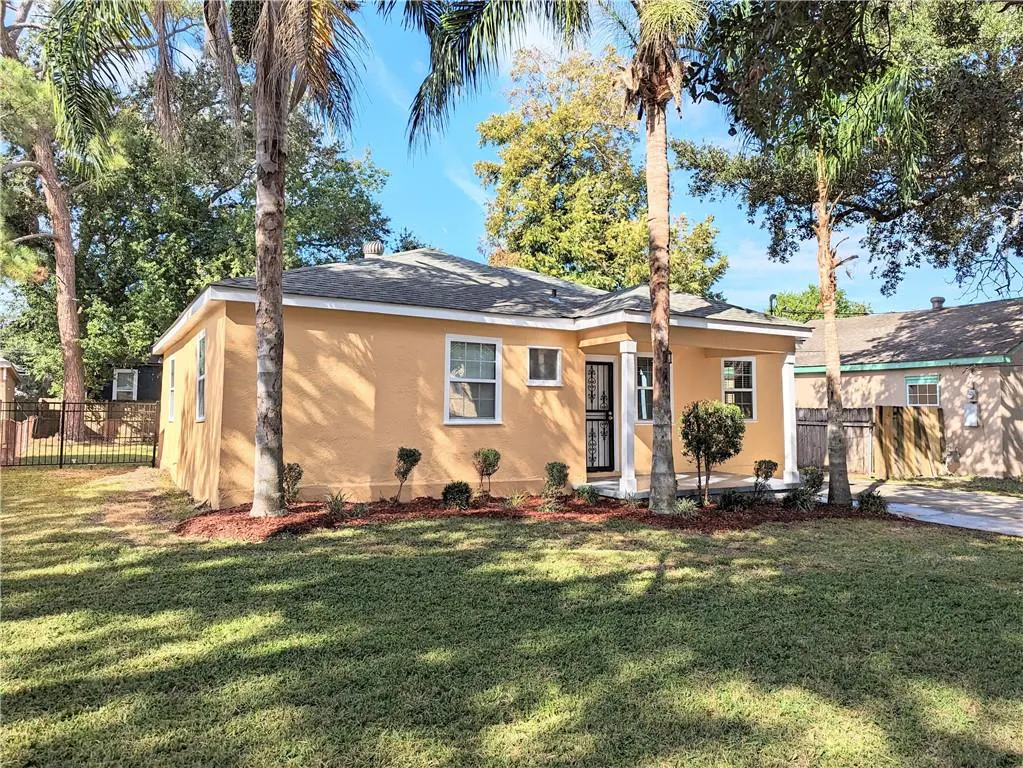 A single-story, light-orange house with a gray roof, white trim, and a green lawn on a sunny day. Palm trees frame the view.
