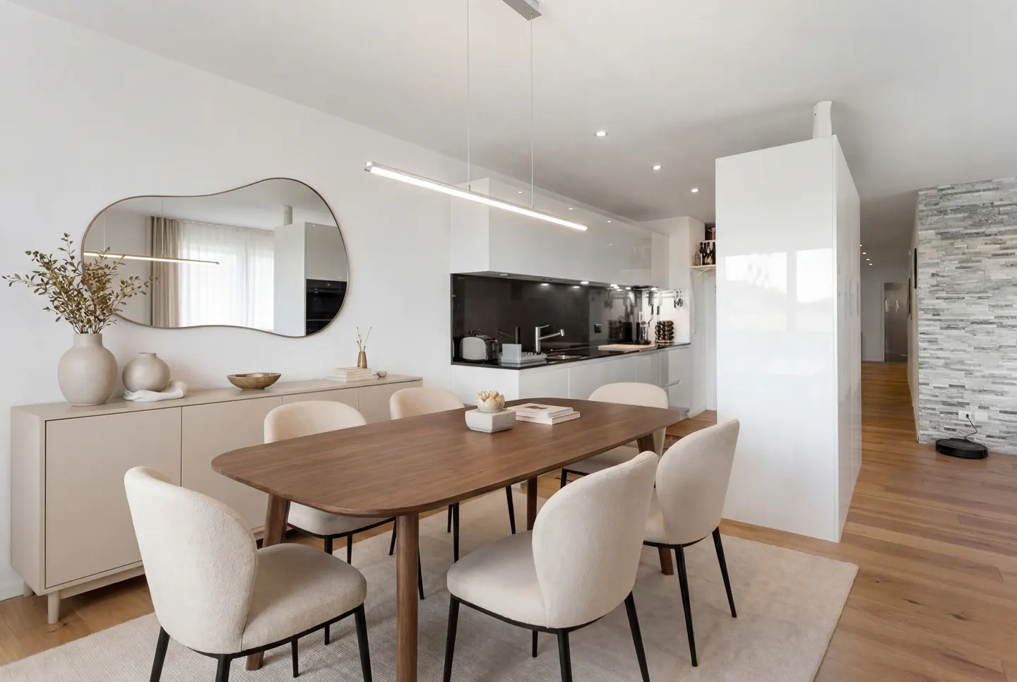 Modern dining area with a wooden table, four cream chairs, a beige sideboard, and an adjacent sleek white kitchen.