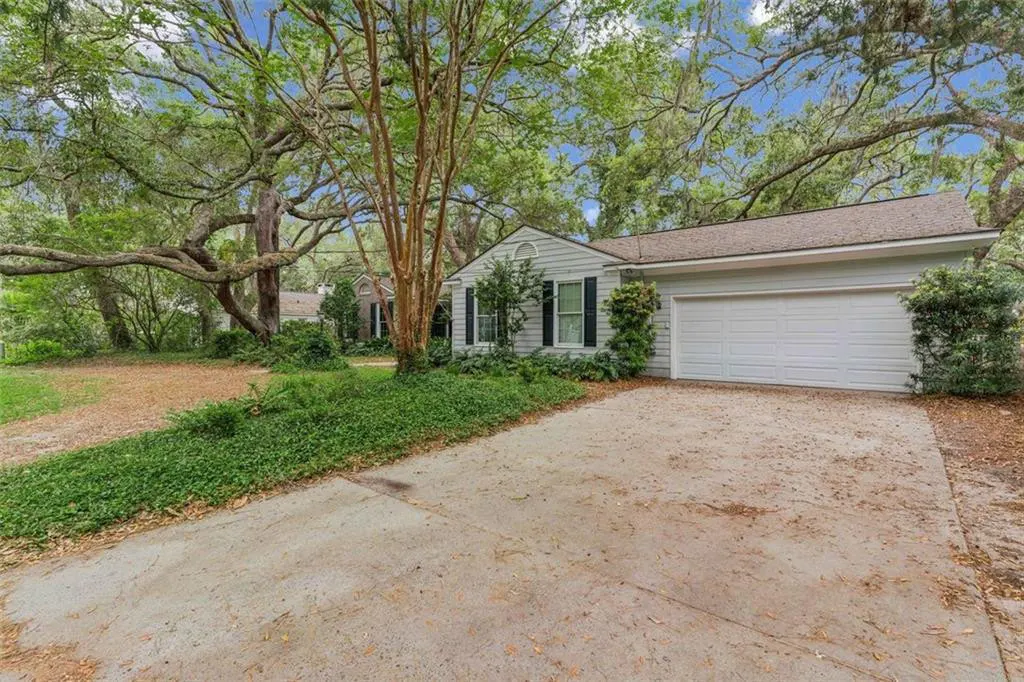 A white house with black shutters and a two-car garage is surrounded by green trees.