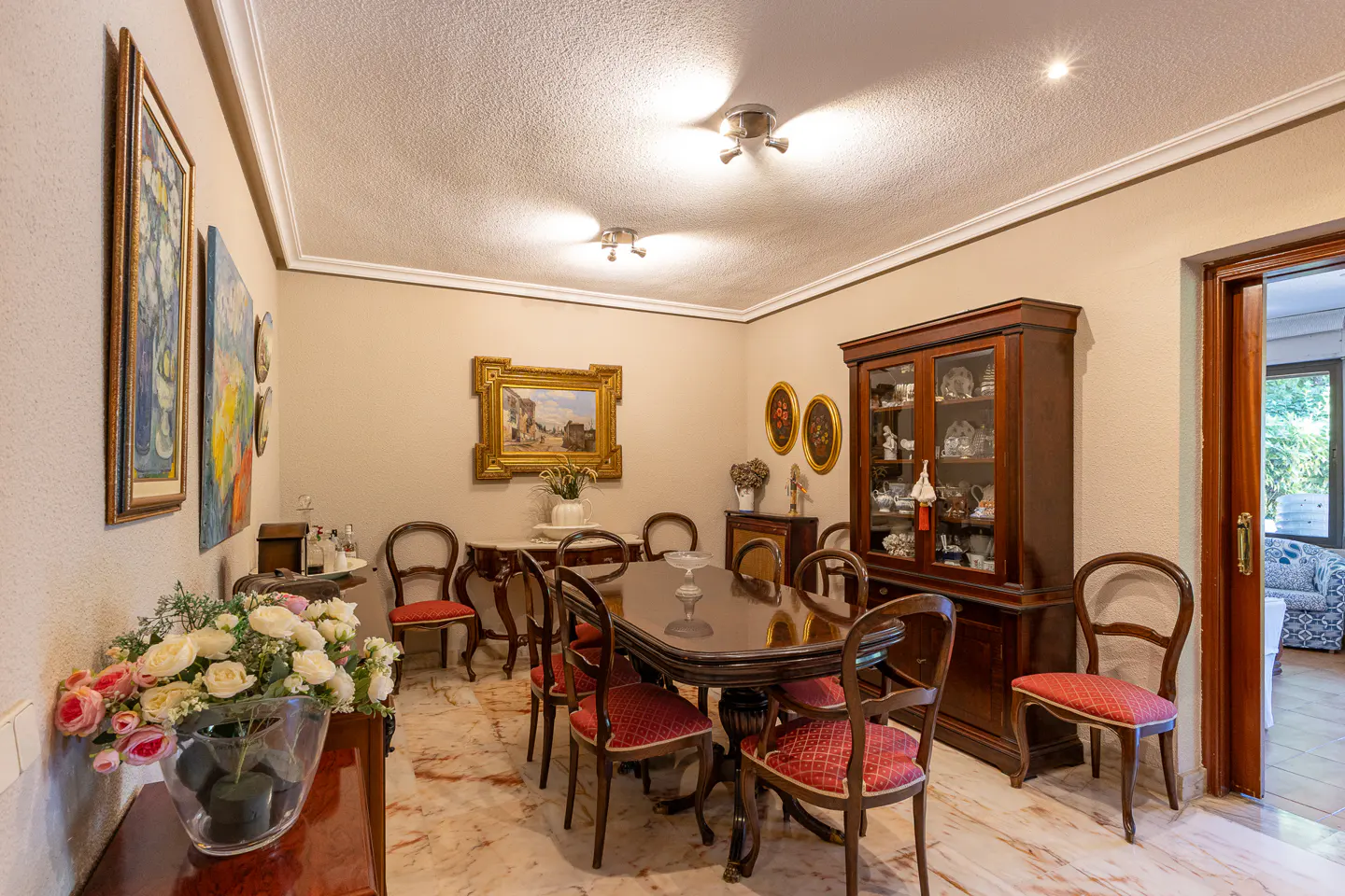 Dining room with a dark wood table, six chairs with red patterned seats, a matching china cabinet, and marble flooring.