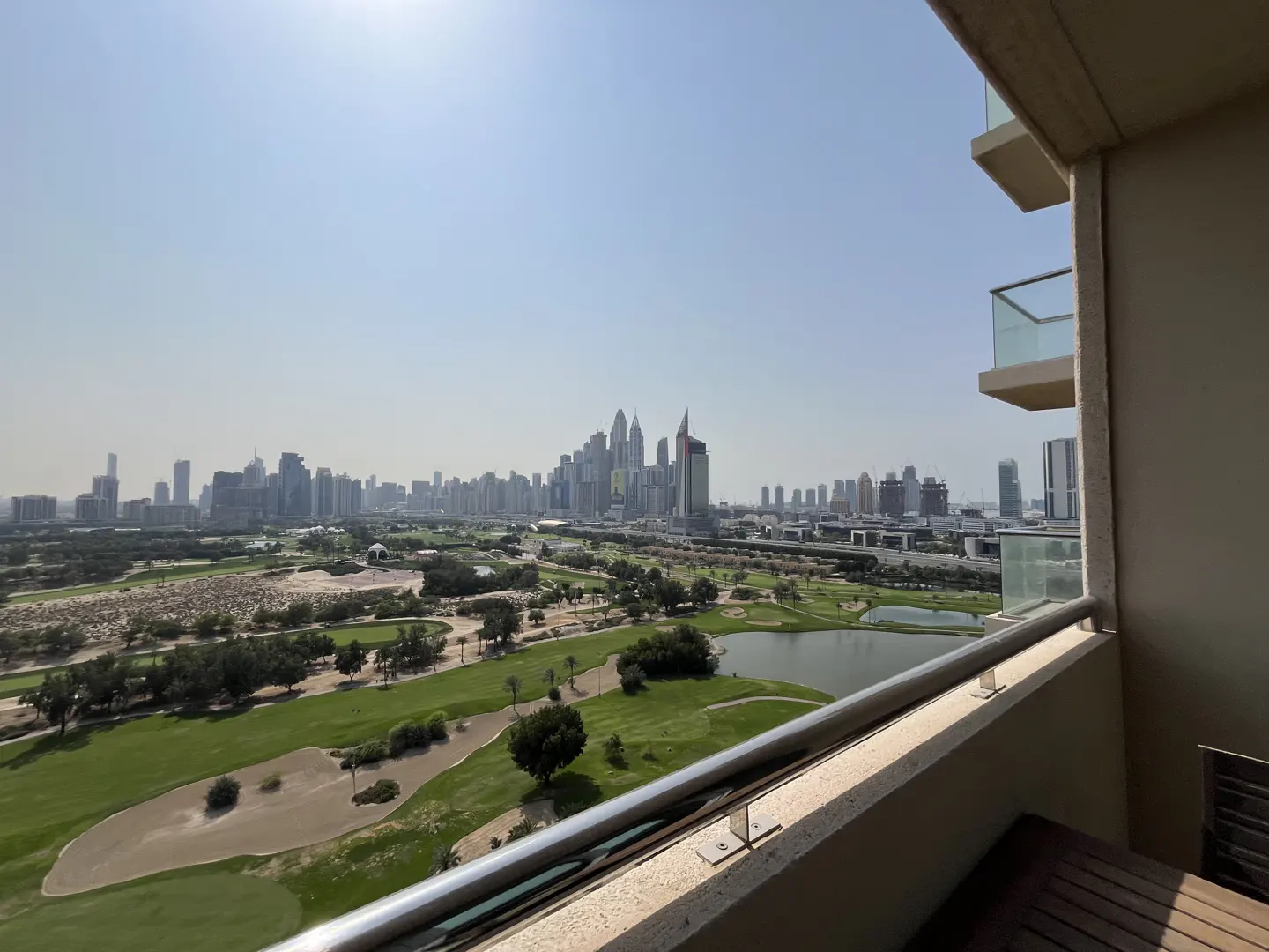 View from a balcony overlooking a green golf course and a city skyline under a clear sky.