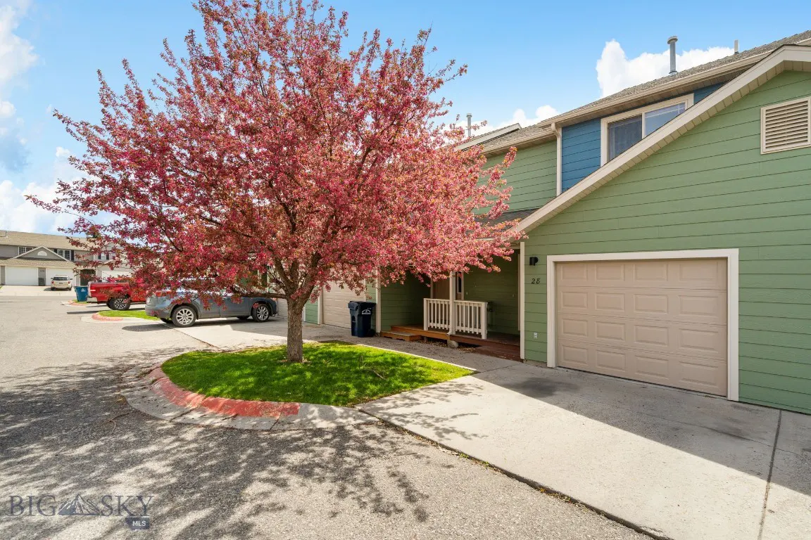 Exterior view of a green townhouse with a beige garage door and a pink flowering tree in the front yard.