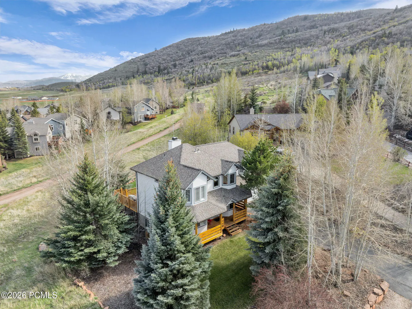 Aerial view of a two-story house with a gray roof, surrounded by pine trees and a mountain backdrop.