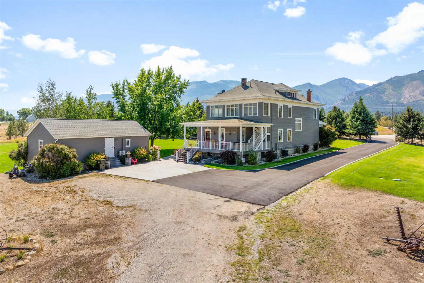 Two-story gray house with white trim and a porch, next to a gray garage, with mountains in the background.