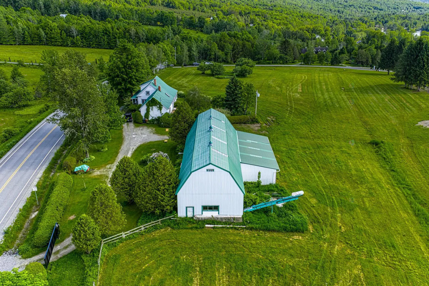 Aerial view of a white barn with a green roof, a white house, and green fields.