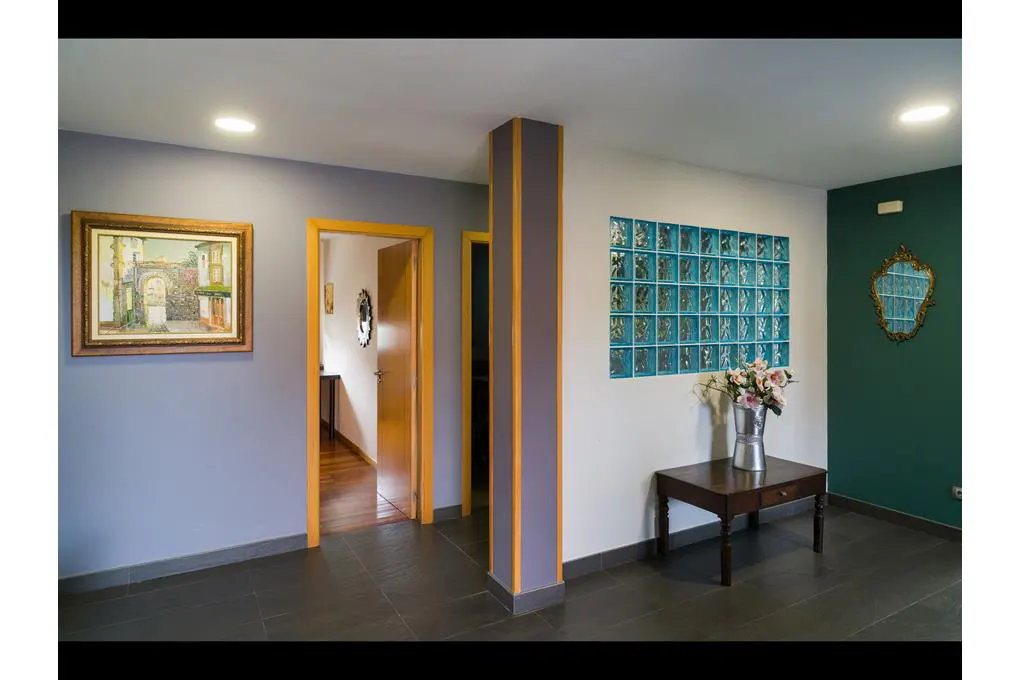 Hallway with gray walls, dark tile floor, and two open doorways. A painting hangs on the left wall, and a table with flowers sits on the right.