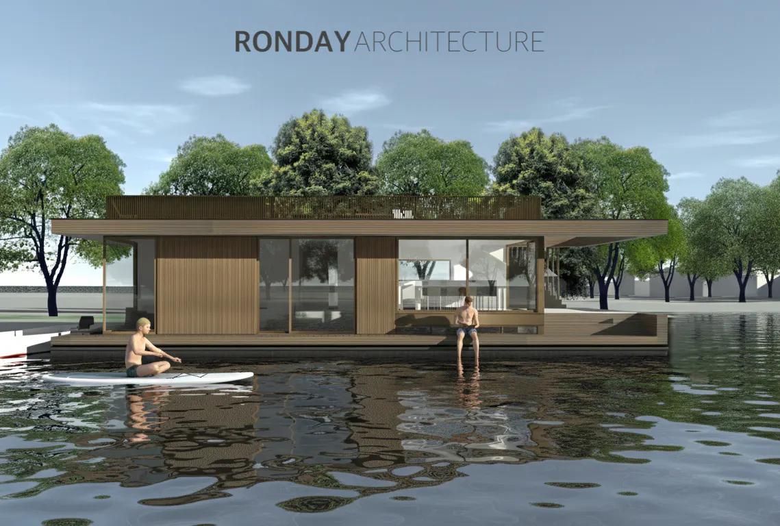 Floating house with wood siding on a lake. A man sits on a paddle board, and another sits on the edge of the deck. Trees in the background.