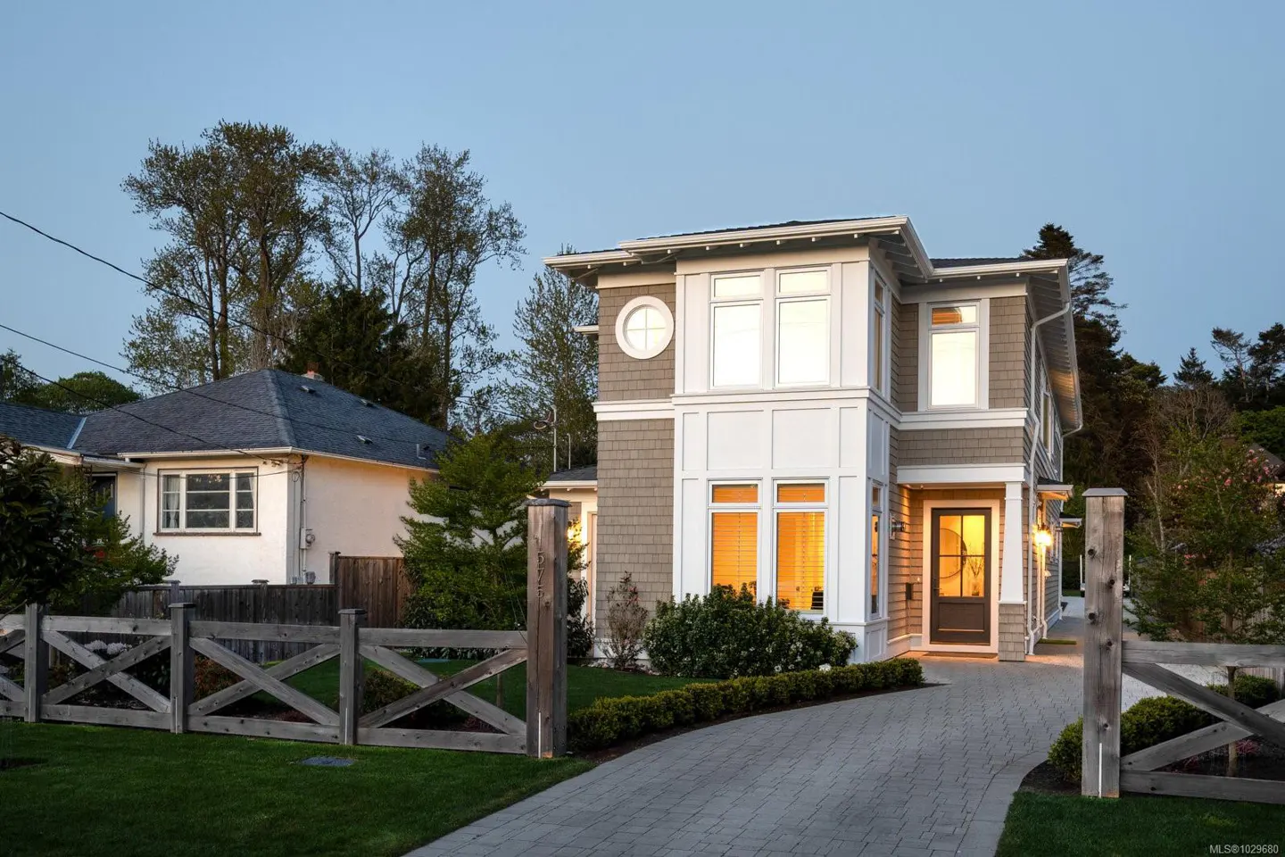 Two-story house with gray shingles and white trim, a gray brick driveway, and a wooden fence.