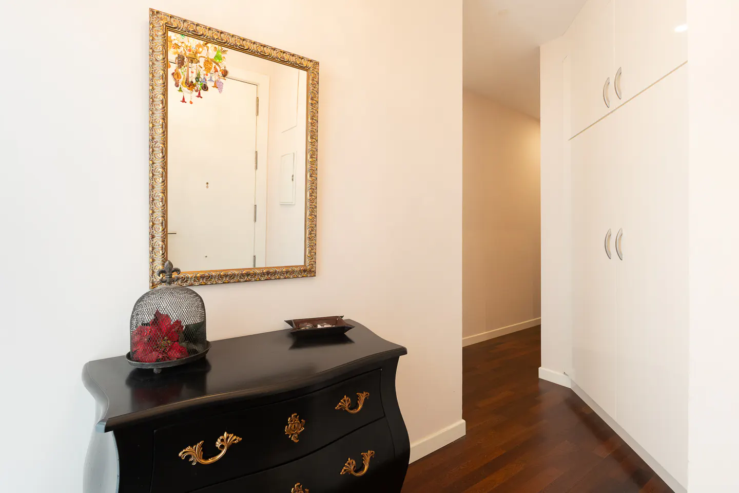 Hallway with a black dresser, gold framed mirror, and white cabinets.
