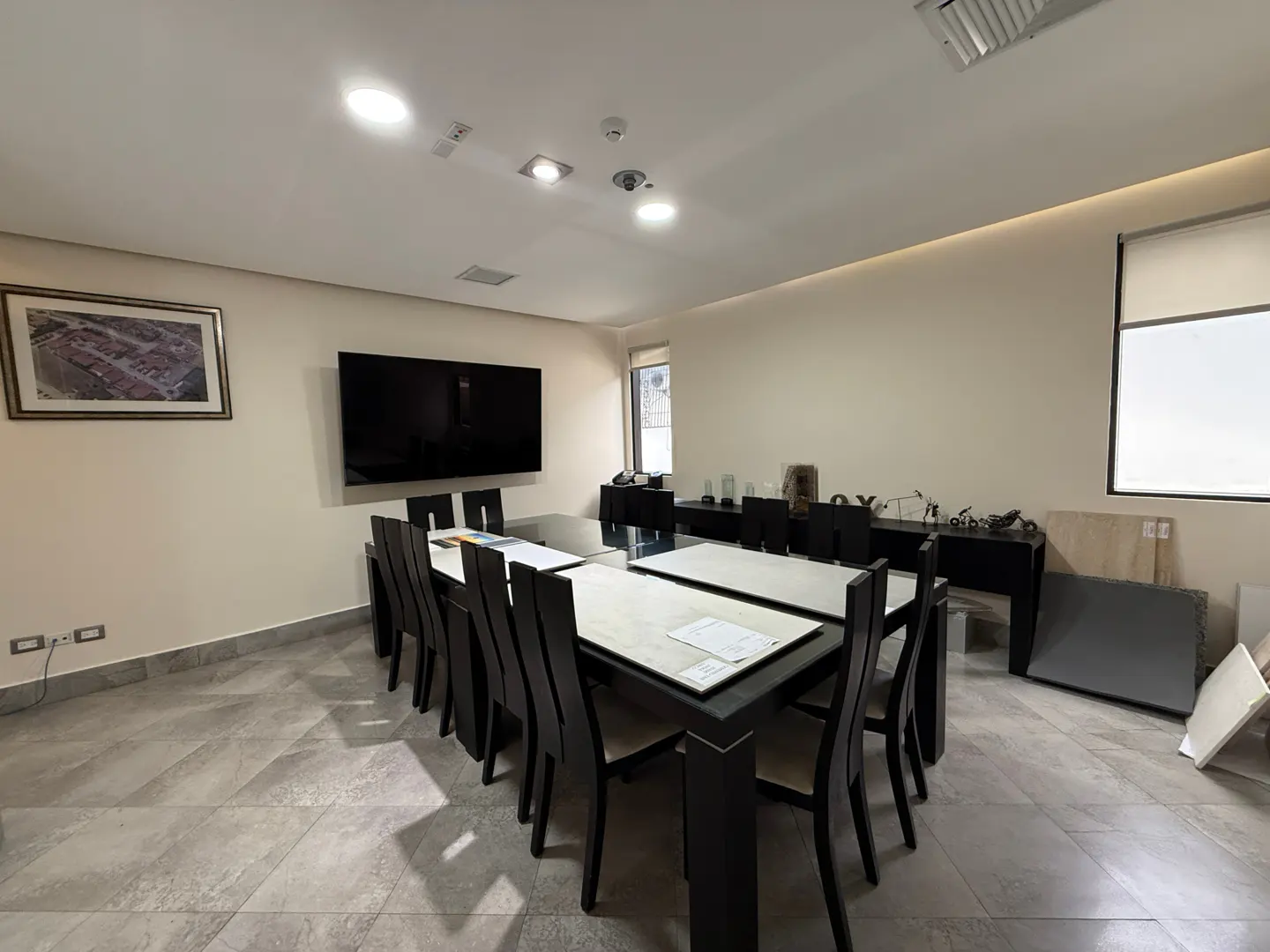 Conference room with a long table, black chairs, and a large TV on the wall. A picture hangs above the table.