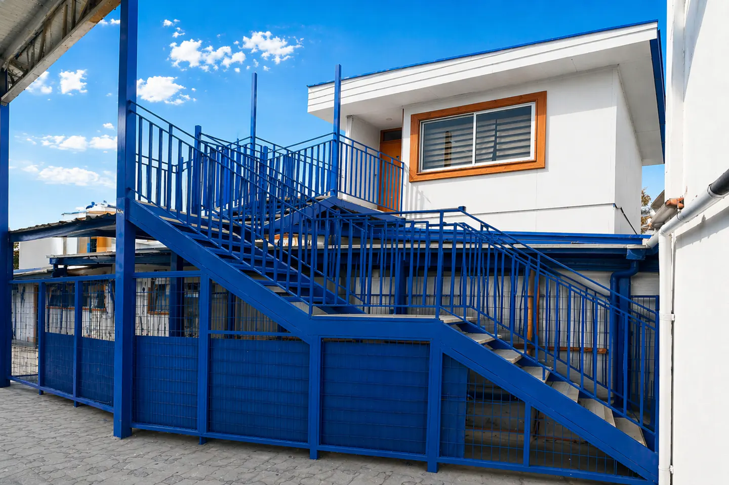 Exterior view of a two-story white building with a blue metal staircase and railing leading to the second floor.