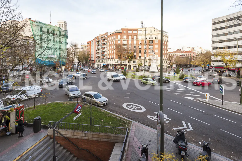 Cityscape view of a busy intersection in Madrid, Spain, with cars, buildings, and a Metro entrance.